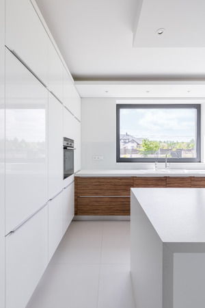 Contemporary, white kitchen with island, wooden cupboards and windowの写真素材