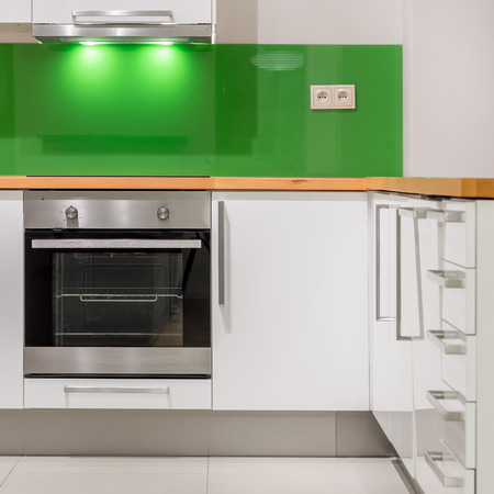 Kitchen with modern, white furniture, green backsplash, wooden worktop and new ovenの写真素材