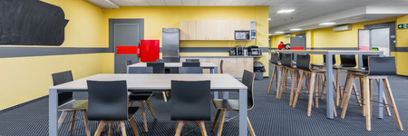 Panorama of modern lunchroom interior with wooden tables and black chairs, kitchenette in backgroundの写真素材