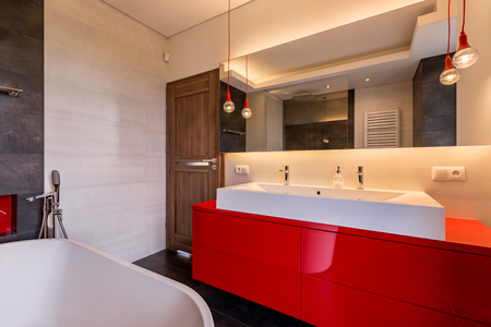 Modern bathroom with red cabinet, bathtub, double basin and mirrorの写真素材
