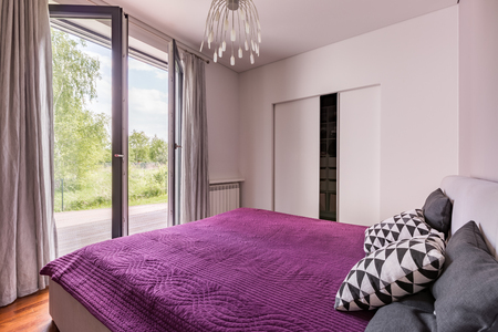 Elegant bedroom with double bed, violet bedding, closet and balconyの写真素材