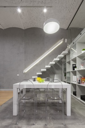 Loft apartment with white table, modern transparent chairs, stairs and brick ceilingの写真素材