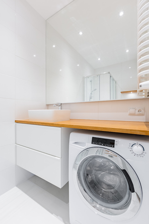 White bathroom with wooden countertop, basin, cabinet, mirror and washerの写真素材