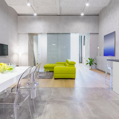 Loft apartment with green couch, table, transparent chairs and glass doorsの写真素材