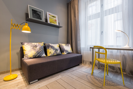 Simple home interior with couch, yellow floor lamp, chair and deskの写真素材