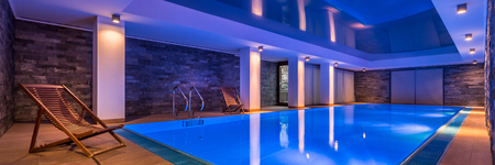 Luxurious indoor swimming pool and stylish, wooden deckchairs, panoramaの写真素材