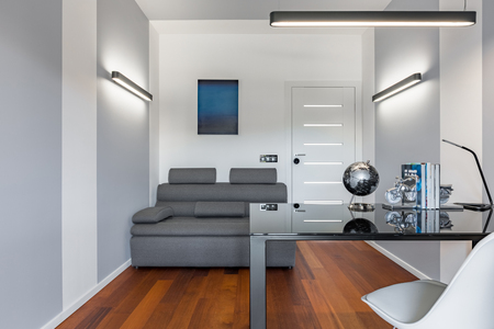 Home office with black glass desk, white chair and gray couchの写真素材