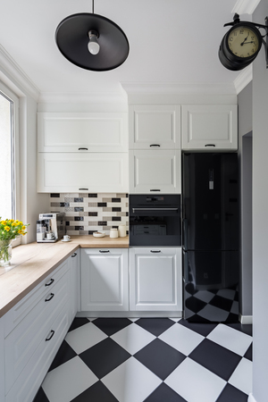 Small, white kitchen with modern chess flooring and black fridgeの写真素材