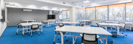 Panoramic view of bright university communal study room with white desks, chairs and big tvの写真素材