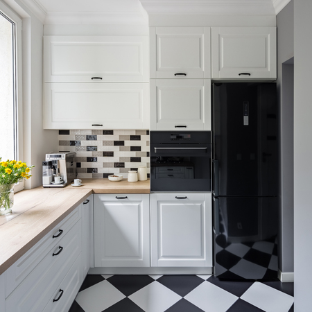 Small, white kitchen with modern chess flooring and black fridgeの写真素材
