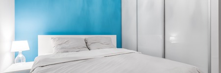 White king size bed in bright bedroom with blue wall, panoramaの写真素材