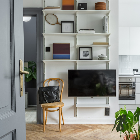 Cane chair next to tv screen, paintings and books on white shelvesの写真素材