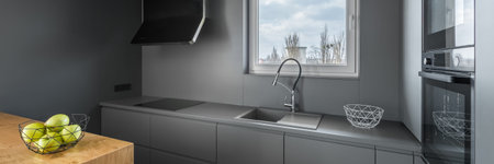 Panorama of gray kitchen with small window, sink and functional cupboards