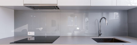 Panorama of white kitchen with gray backsplash, sink and induction hob