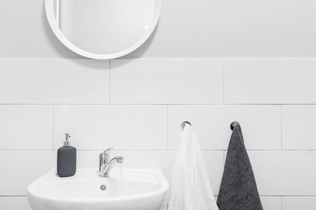 Bathroom with simple, white tiles, small basin and round mirrorの写真素材
