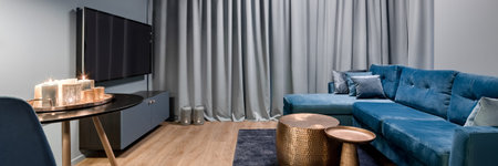 Panorama of elegant living room in blue and gray with big, blue sofa and two copper coffee tables