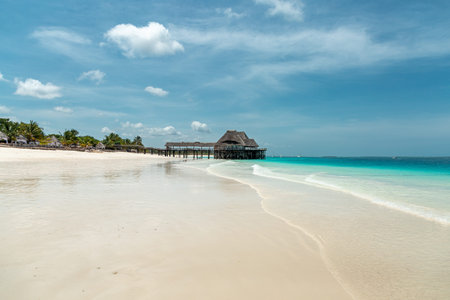 Paradise view of white, wide sand beach and turquoise ocean and palm tree forest and wooden buildingsの写真素材
