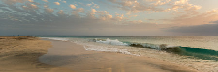Sunrise with sky full of small clouds over blue ocean and wide beach, panoramaの写真素材