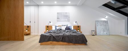 Panorama of attic bedroom with wooden bed, big wardrobe with mirror doors and ceiling windowの写真素材