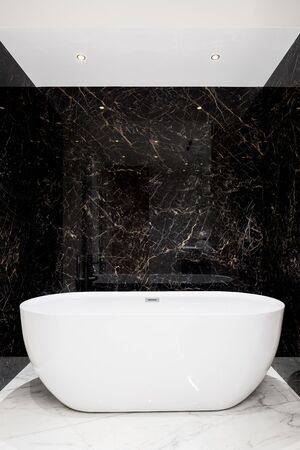 Luxury white bathtub in stylish bathroom with black marble on the walls and white marble tiles on the floorの写真素材