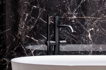 Close-up on stylish black bathtub faucet in bathroom with elegant black marble wallの写真素材