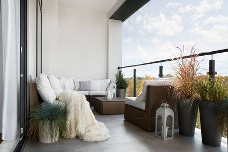 Beautiful decorated balcony with wicker furniture, white pillows and many decorative plantsの写真素材