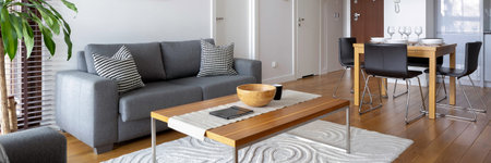 Panorama of modern living room with grey sofa and wooden coffee table open to dining area with table...