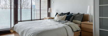 Panorama of stylish bedroom with double comfortable bed and big balcony windows with blinds