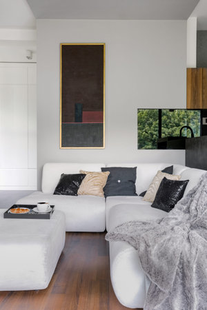 Elegant white corner sofa with decorative pillows and blanket and white ottoman