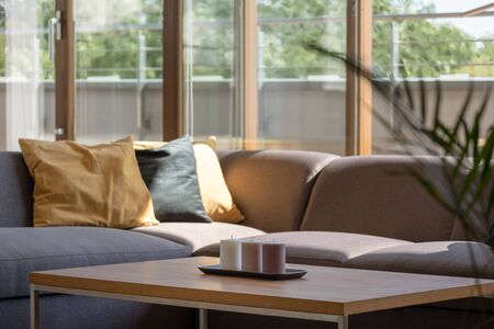 Wooden coffee table and gray corner sofa in living room with window wallの写真素材