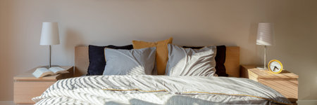 Panorama of stylish bedroom with big, comfortable, double bed and two night tables with lamps