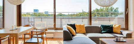 Panorama of elegant living room with wooden dining table, corner sofa with coffee table and big window doors to terrace around roomの写真素材