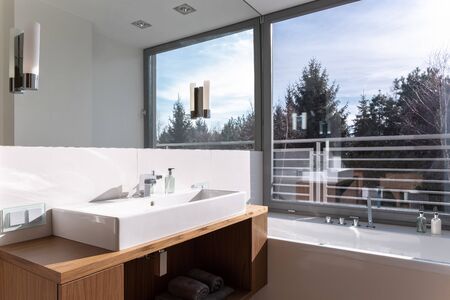 Stylish and bright bathroom with simple washbasin with mirror and big window above bathtubの写真素材