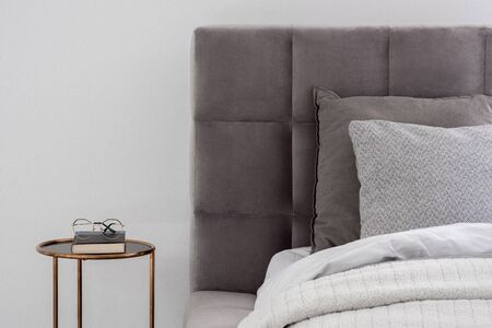 Close-up on gray quilted bed with round, golden bedside table in white wall bedroomの写真素材