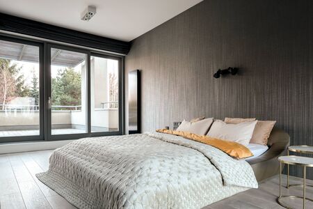 Elegant bedroom with double bed, vinyl wallpaper and balcony behind window wallの写真素材