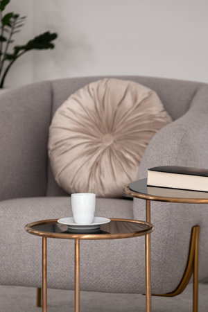 White coffee cup and book on two modern coffee tables and stylish armchair in the backgroundの写真素材