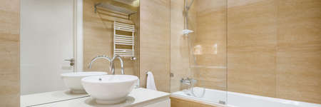 Panorama of elegant bathroom with big bathtub, mirror wall, stylish washbasin and with beige tilesの写真素材