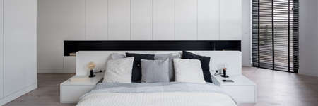 Panorama of modern and elegant black and white bedroom with big bed, many wardrobes and balcony window with black blindsの写真素材