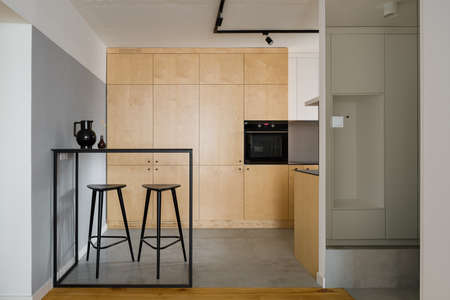 Modern style kitchen with birch plywood cupboards, black table with tall bar stools and concrete wall and ceilingの写真素材