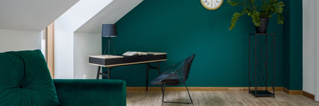 Panorama of stylish attic room with emerald green on the wall and sofa, and with stylish black desk...