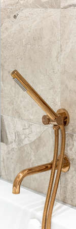 Vertical panorama of copper bathtub faucet and shower handle in bathroom with marble tiles, close-upの写真素材