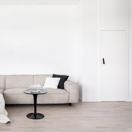 Living room with white wall and door, beige sofa and black modern coffee table