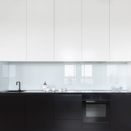 Elegant and simple kitchen with black lower drawers, cupboards and countertop and white higher...