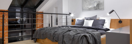 Panorama of modern bedroom on mezzanine in loft style apartment with big window and brick wall at...