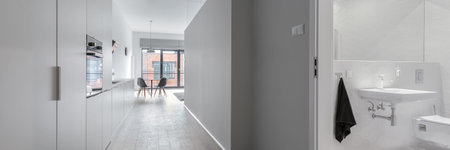 Panorama of stylish corridor in apartment with gray walls and open doors to modern bathroom in white