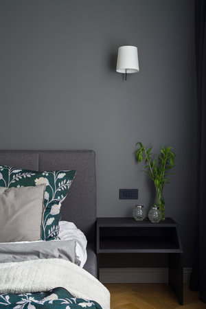 Bedroom with stylish gray wall, bed and black bedside table with decorations