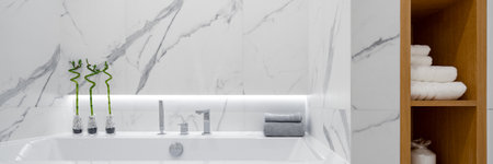 Panorama of simple bathtub in elegant and bright bathroom with white marble tiles and wooden shelves for towelsの写真素材