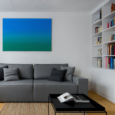 New design in living room with white walls, art, white bookcase, simple gray couch and square, black coffee tableの写真素材