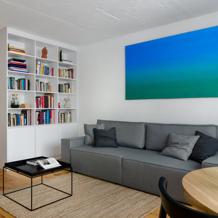 Small and comfortable living room with white bookcase, pine wood floor, big gray couch and big paintingの写真素材