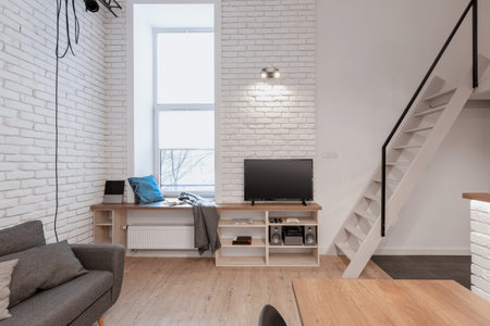 Loft style apartment with stairs to mezzanine from tv room with narrow window and white brick on the wallsの写真素材